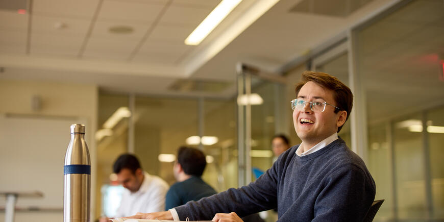 PhD student Alex Busch sits in a classroom smiling up at someone off screen