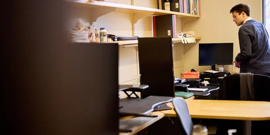 PhD student Alex Busch stands at his desk surveying a stack of books