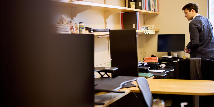 PhD student Alex Busch stands at his desk surveying a stack of books