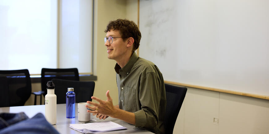 Associate Professor Nathan Wilmers sits at a table in a classroom talking to students who are offscreen