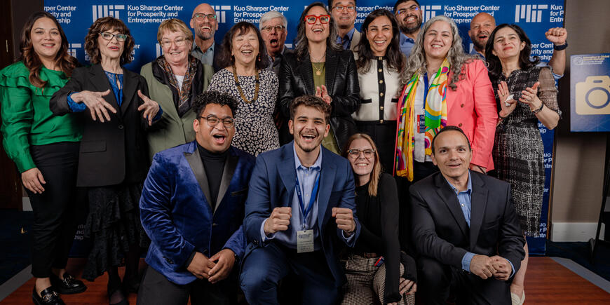 A group of 15 people in business wear, smiling in front of a blue and white MIT backdrop