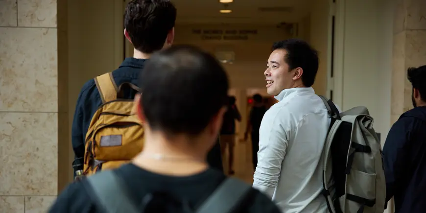 Patrick Yeung walks down the halls of MIT Sloan, away from the camera, and turning to his side to speak with another student