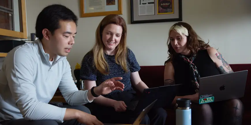 Patrick Yeung and two other people sit on couches with laptops. They all look at Patrick's laptop, talking about what they see there