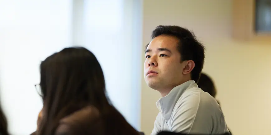 Patrick Yeung sits in a conference room with other students. He look intently at something outside the frame