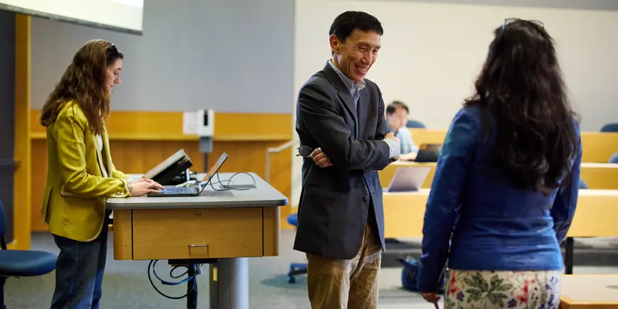 Professor Yasheng Huang stands at the front of a lecture hall speaking with a student