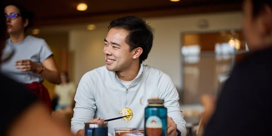Patrick Yeung sits in the MIT Sloan Cafe eating lunch. He smiles at someone off camera