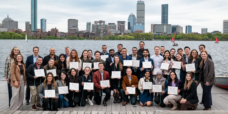 students pose in front of the Boston skyline with graduation certificates