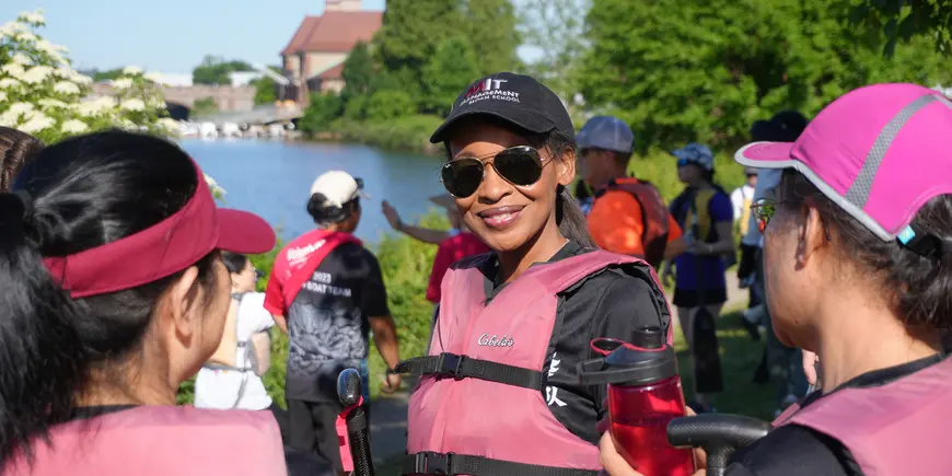 A smiling woman wearing sunglasses and a lifejacket listens to a group