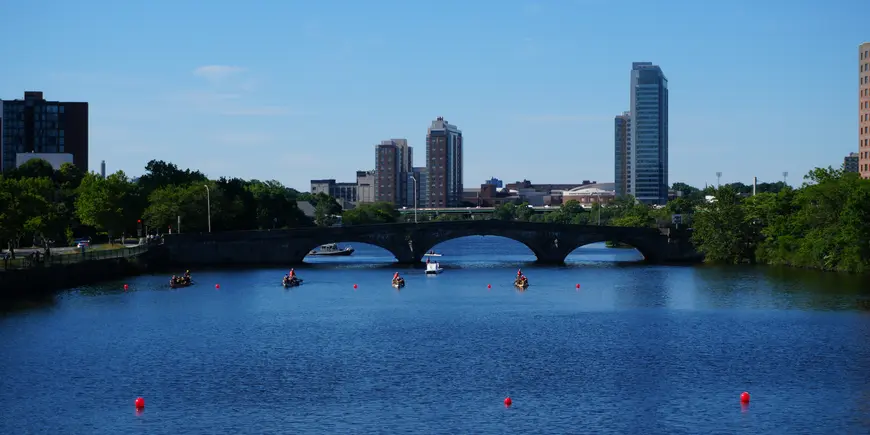 Several boats move across the Charles River in front of Boston skyline