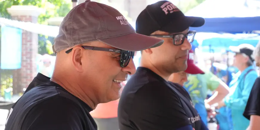 Two men smile and listen to others speaking offscreen