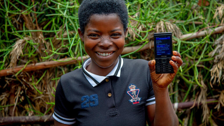 A child holds a phone displaying the GiveDirectly cash payment system.
