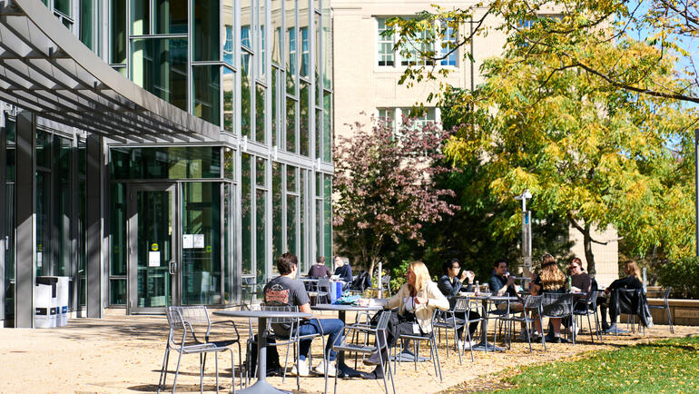 Students sit outside of E62 on a sunny day
