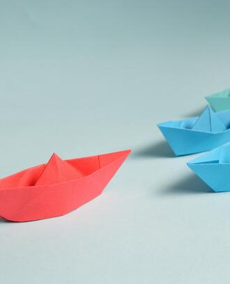 Paper origami boats on light blue background