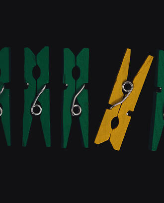 A yellow clothes pin among a row of green ones