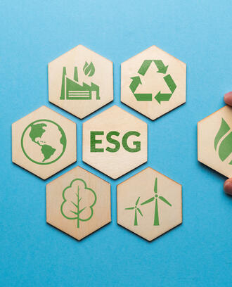 Hand pulling a hexagonal wooden tile away from a group of six other tiles with ESG in the middle