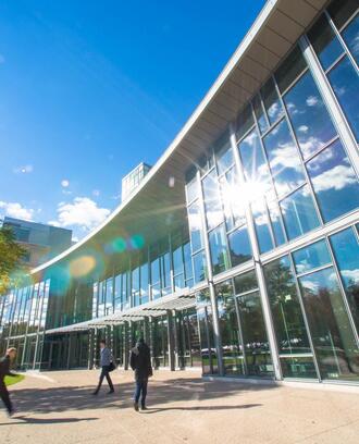 The outside of the MIT Sloan building E-62, on a sunny day with people walking near it