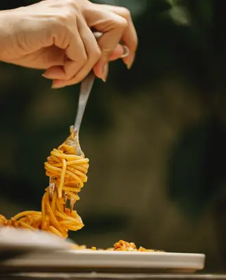 Image of a hand holding a fork with spaghetti swirled around it
