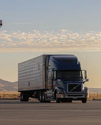 White freight truck on road with mountain range in the background.