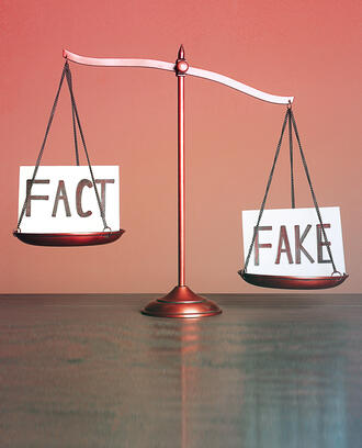 A justice scale has the word "Fact" on one side and "Fake" on the other.
