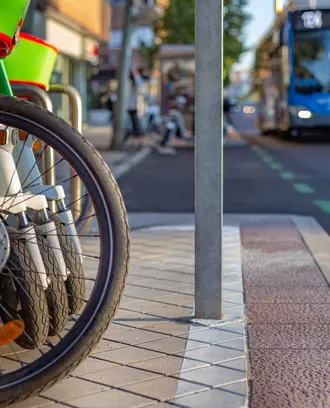 Rental bikes and scooters parked on sidewalk with bus on the road in background