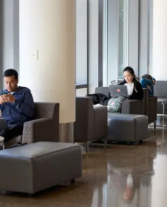 Chairs by the windows near the e62 cafe with a few students sitting and working