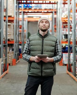 Image of a young man in a down vest holding a computer tablet in a warehouse setting