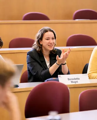 Female student speaking in class sitting between two students.