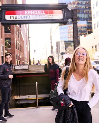 Three MIT Sloan students facing the camera with backs turned toward the MBTA station stairs outside in Kendall Square.