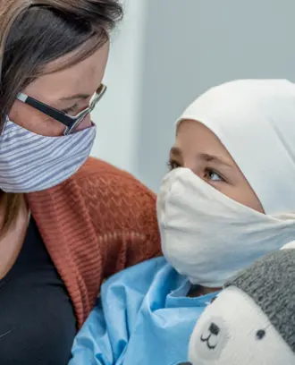 A mother hugs her young daughter while she receives cancer treatment