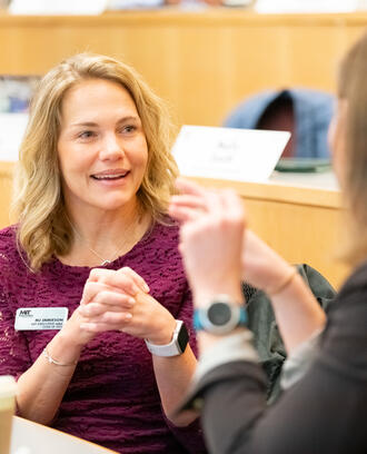 MJ Jamieson, EMBA '25, talking to a classmate, hands clasped.