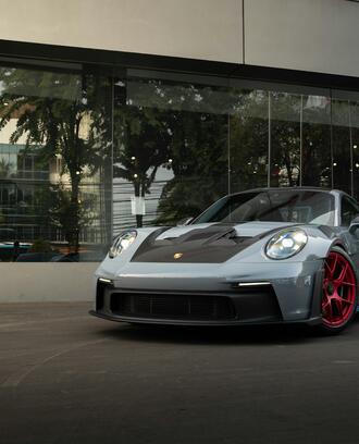 Photo of silver Porsche with a black hood and red rims parked outside of a glass storefront.