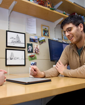 PhD student Ben Manning sits at a desk in the MIT Sloan PhD offices. He looks down at a tablet, talking to someone out of frame.