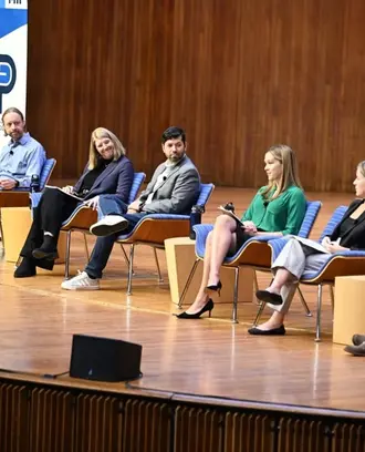 Image of 6 panelists sitting on stage while one speaks.