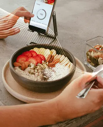 A person eats a healthy breakfast while looking at a phone app