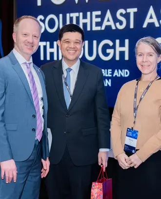 Three people smile and pose for a picture in front of a stage