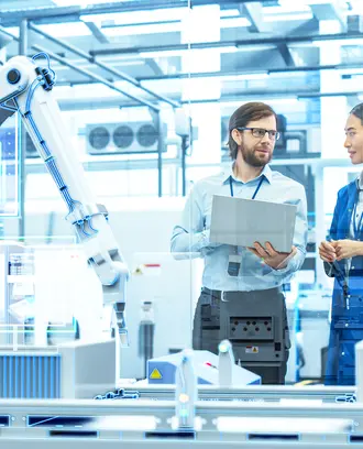 Employees in discussion inside a manufacturing plant with robotic arms and digital screens