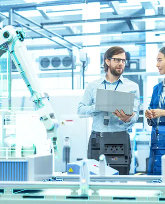 Employees in discussion inside a manufacturing plant with robotic arms and digital screens