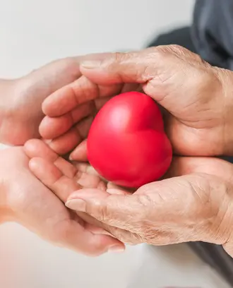 Two pairs of hands holding a red heart