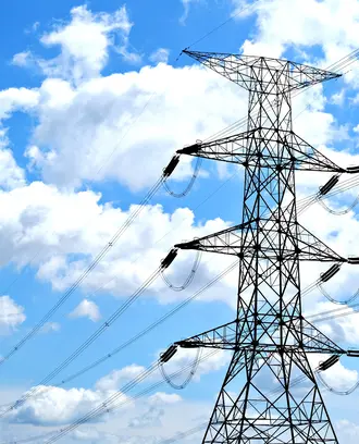 Electricity pylon with high voltage lines set against a vibrant blue sky with clouds.
