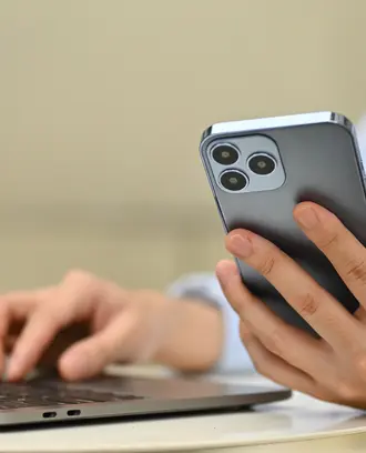Close-up image of an unrecognizable businessman using a mobile phone and laptop, remotely working from outside