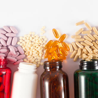 five brightly colored pill bottles on their sides with different sized pills spilling from each