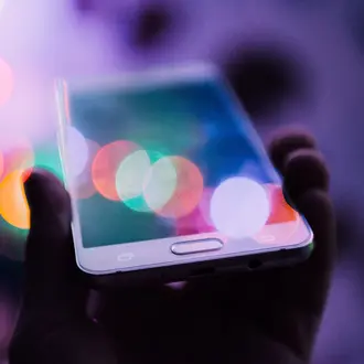 Hand holding a smartphone with lots of colors coming off the screen.