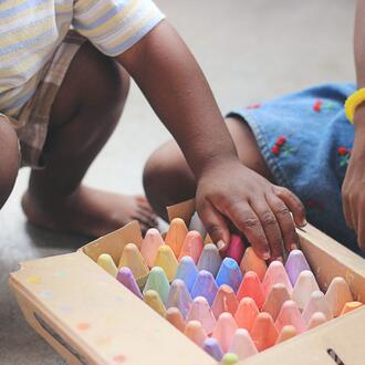 Two children kneeling over a wooden box of colorful chalk