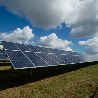 Solar panels in a field under a blue sky with clouds.