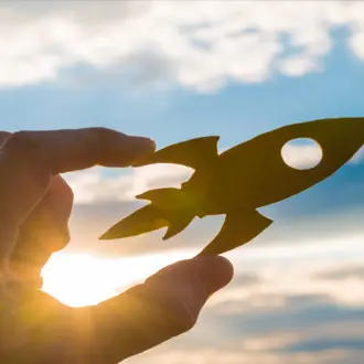 Hand holding small rocket ship against the sky.