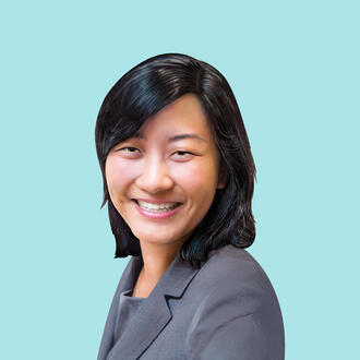 Kristin Kagetsu, co-founder of Saathi, faces the viewer and smiles. She stands in front of a light blue background and she is wearing a gray suit coat.
