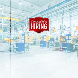 A hiring sign hangs on doors to a manufacturing plant