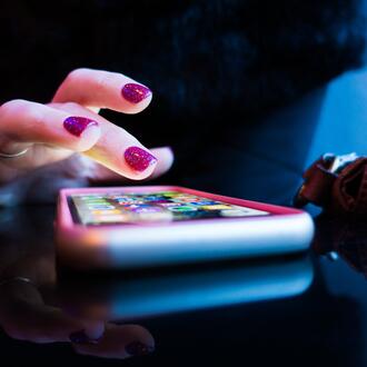 Hand with pink nail polish hovering over cell phone on table