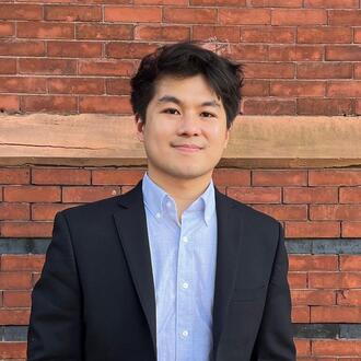 Headshot of MIT  Sloan PhD student Zach Tan, wearing a blazer jacket and blue shirt