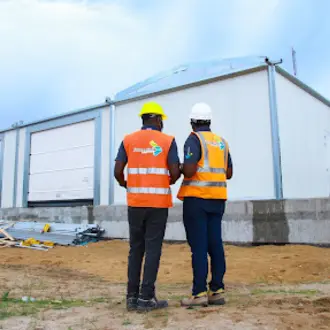 photograph of two men in high-vis vests and hard hats standning infront of a newly built warehouse
